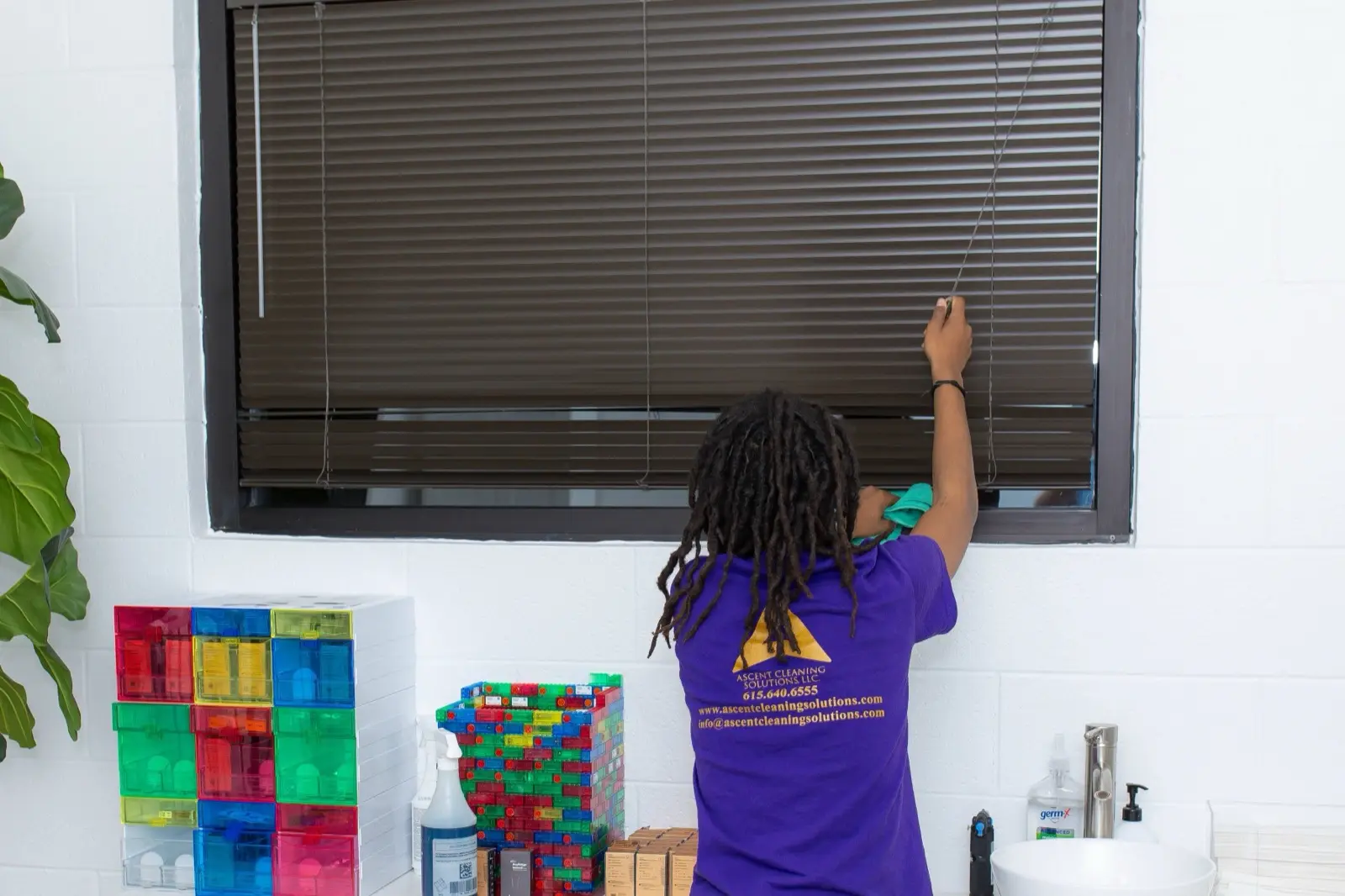 Ascent Cleaning Solutions team member in branded uniform cleaning blinds in a Nashville daycare facility